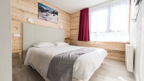 A bedroom with a bed, wooden walls, a window with curtains, and a painting on the wall. - Vacances Bleues Arc En Ciel Les Karellis (Montricher-Albanne)