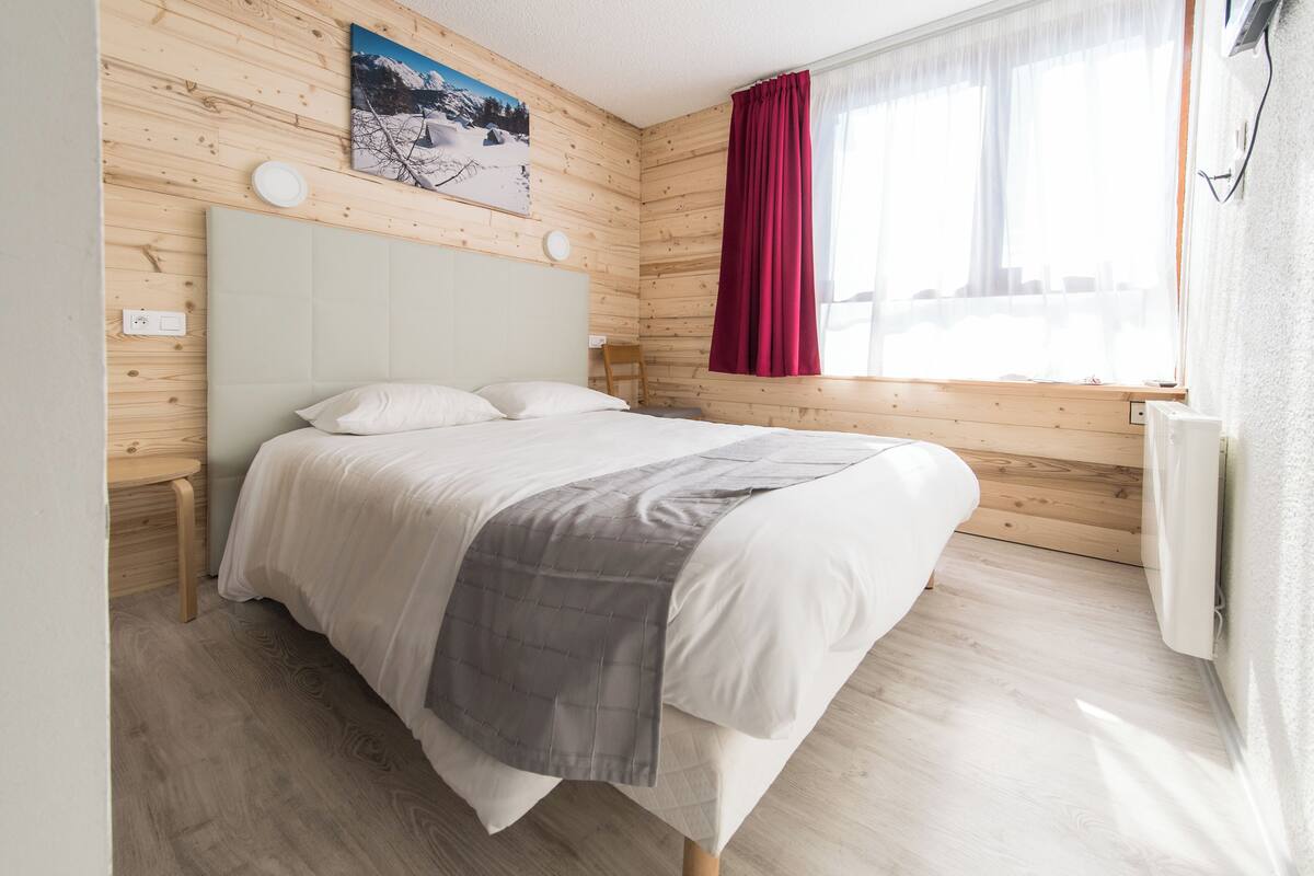 Une chambre à coucher avec un lit, des murs en bois, une fenêtre avec des rideaux et un tableau accroché au mur.