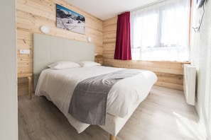 Un dormitorio con cama, paredes de madera, una ventana con cortinas y un cuadro en la pared.
