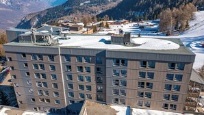 A multi-story hotel with a flat roof, large windows, and a view of a snowy landscape with mountains in the background. - Vacances Bleues Arc En Ciel Les Karellis (Montricher-Albanne)