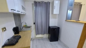 A compact kitchen with a stove, sink, and a small trash bin.