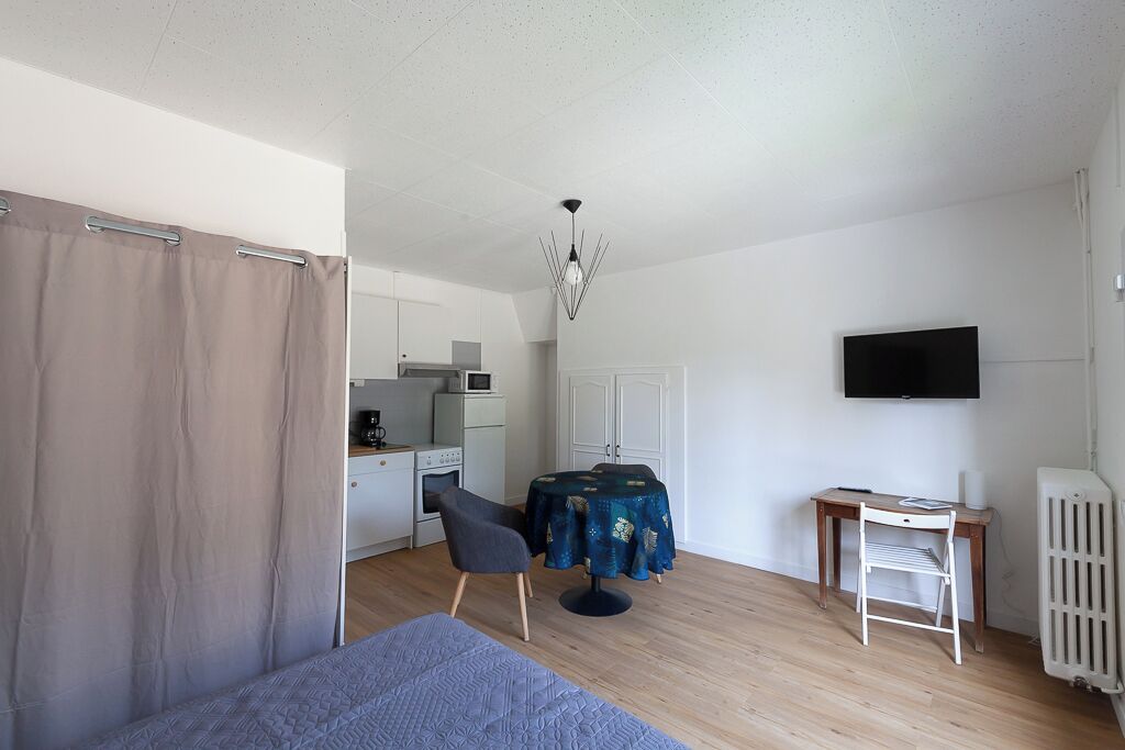Une pièce de taille modeste comprenant un lit, un bureau, une chaise, une table, un téléviseur et un coin cuisine.