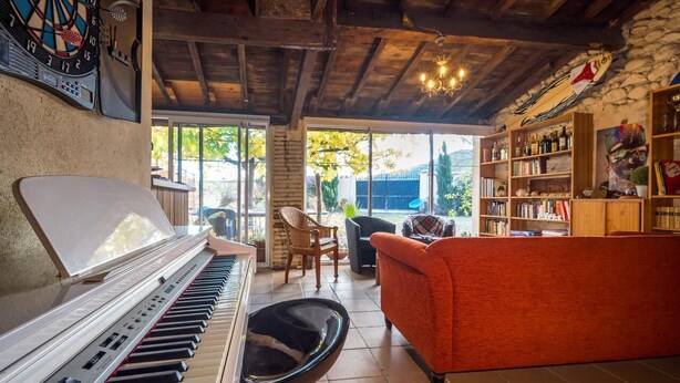 Ein gemütliches Wohnzimmer mit einem Klavier, einem roten Sofa und einem Bücherregal voller Bücher und Dekoration.