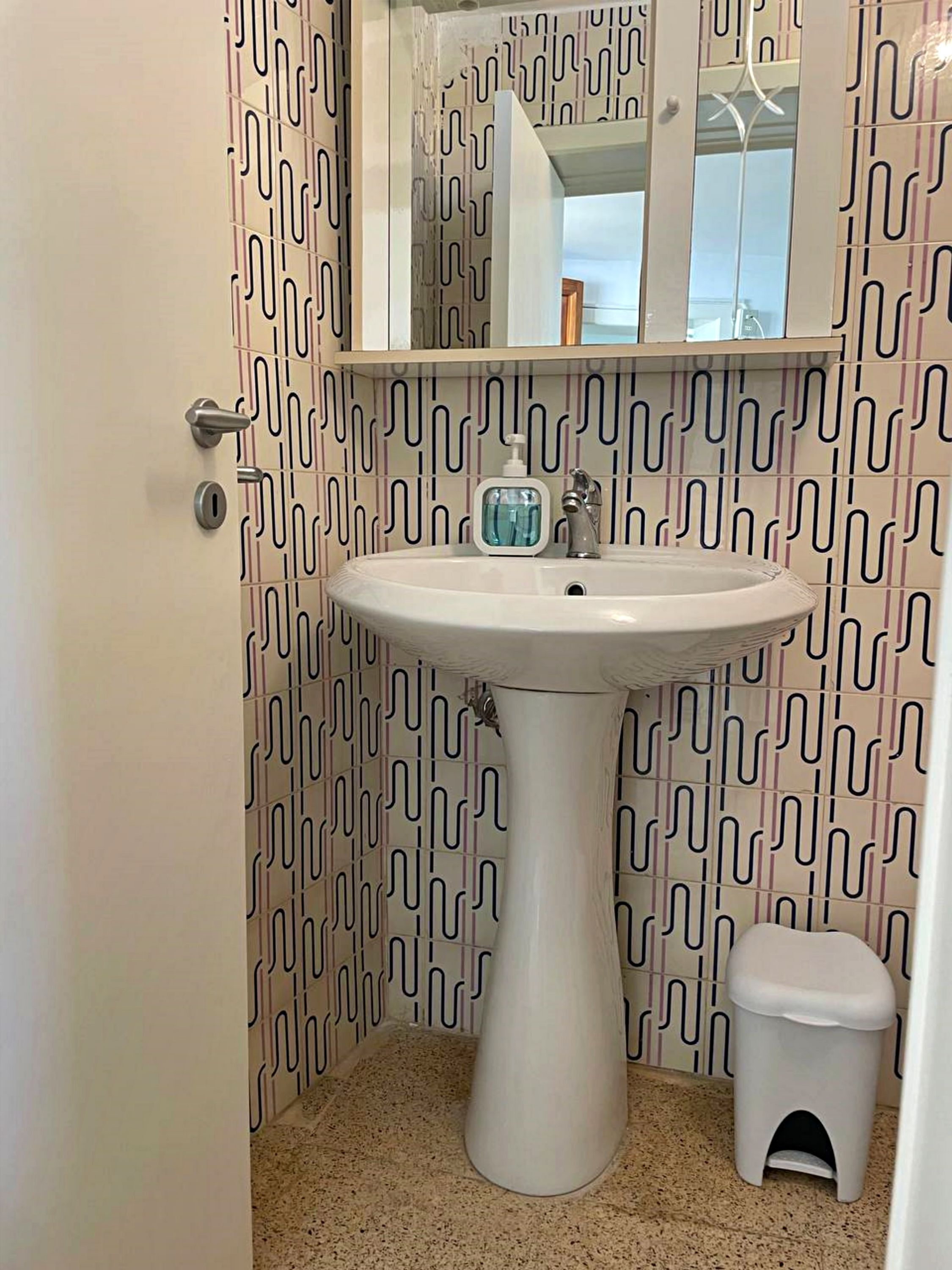 A bathroom with a white sink, a small stool, and a mirror above the sink.