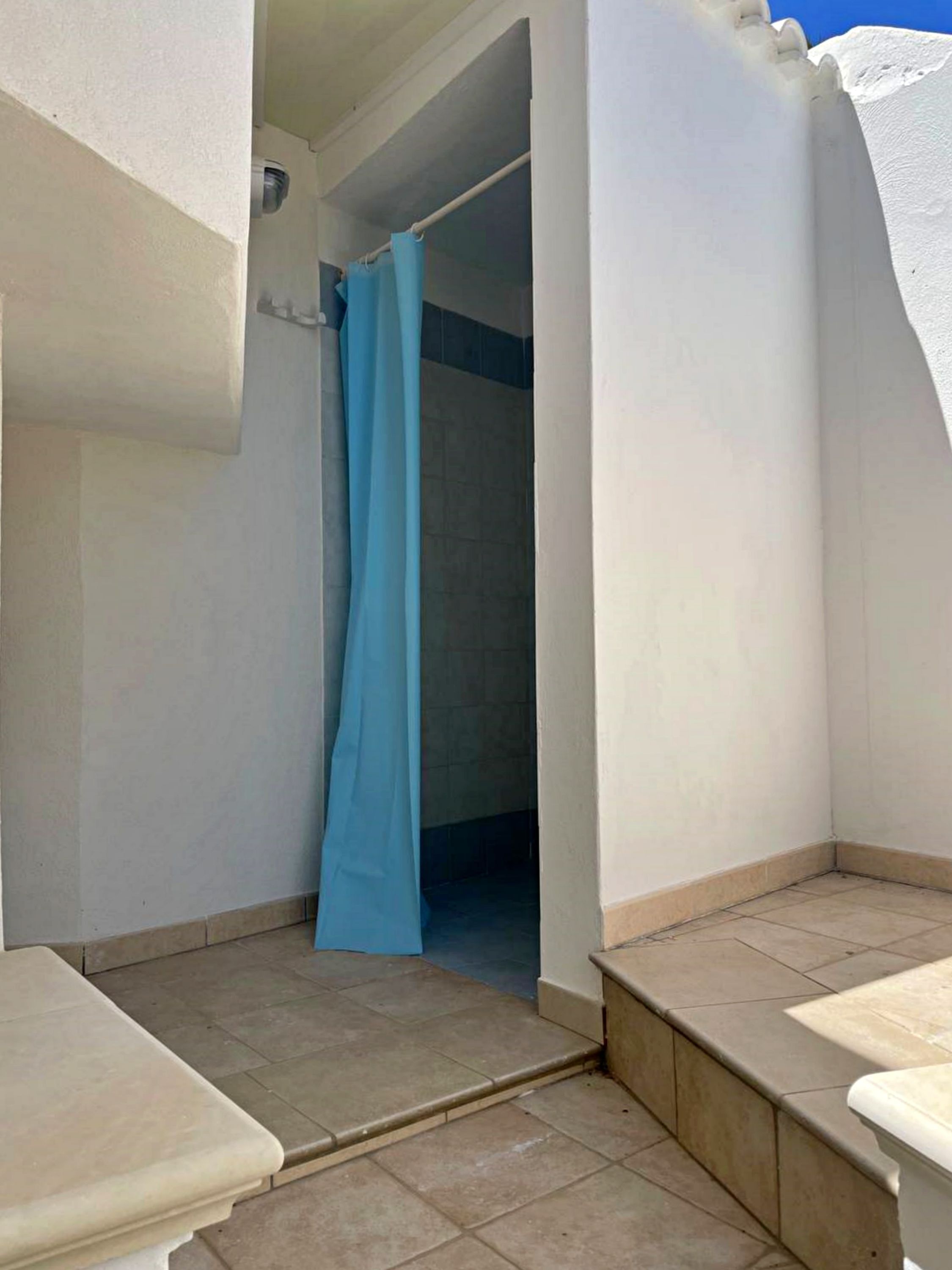 A small, enclosed bathroom with a shower area, tiled floor, and white walls.