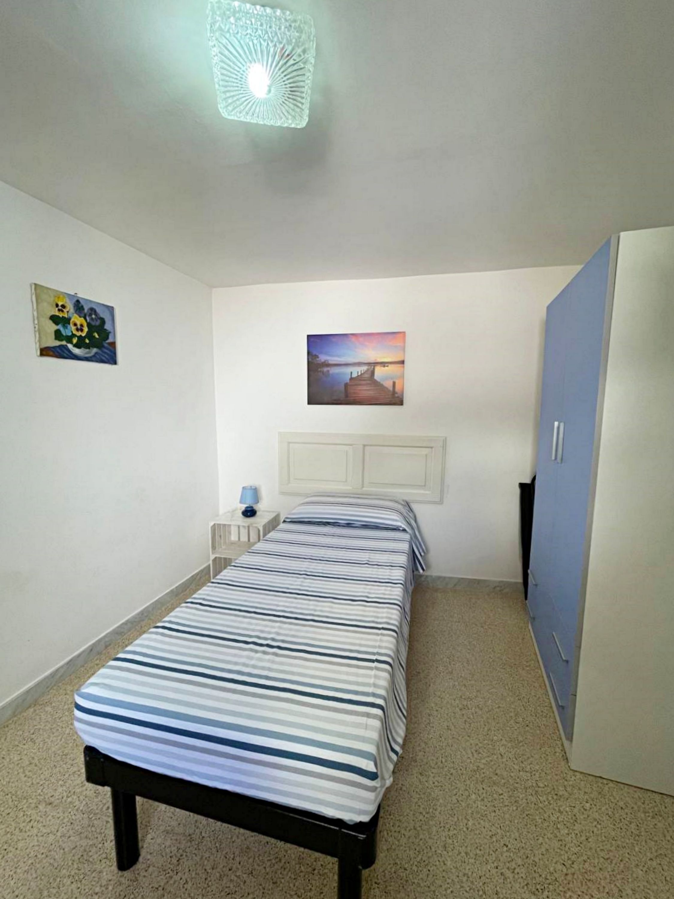 A bedroom with a bed, a nightstand, a lamp, a painting, and a wardrobe.