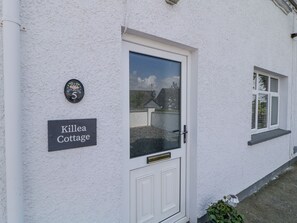 Ein weißes Cottage mit Tür und Fenster. An der Wand ist ein Schild mit der Aufschrift "Killea Cottage".