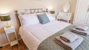 Una cama bien hecha con un cabecero verde acolchado, una lámpara de noche y una toalla doblada sobre la cama.