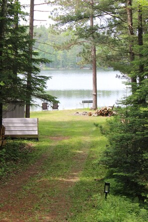 A lakeside cabin with a dock, a bench, and a pile of firewood. - Classic Rustic Lakeside Cabin Retreat. Sleeps 6. Pets allowed. (Winter)