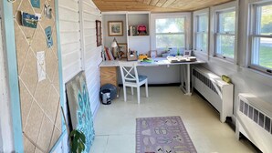 Une cuisine de taille réduite avec un plafond en bois, un bureau blanc et une chaise. On y trouve des fenêtres, un radiateur et un petit tapis sur le sol.