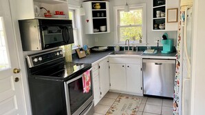 Une cuisine avec des meubles blancs, une cuisinière noire, un four à micro-ondes, un évier et un lave-vaisselle.