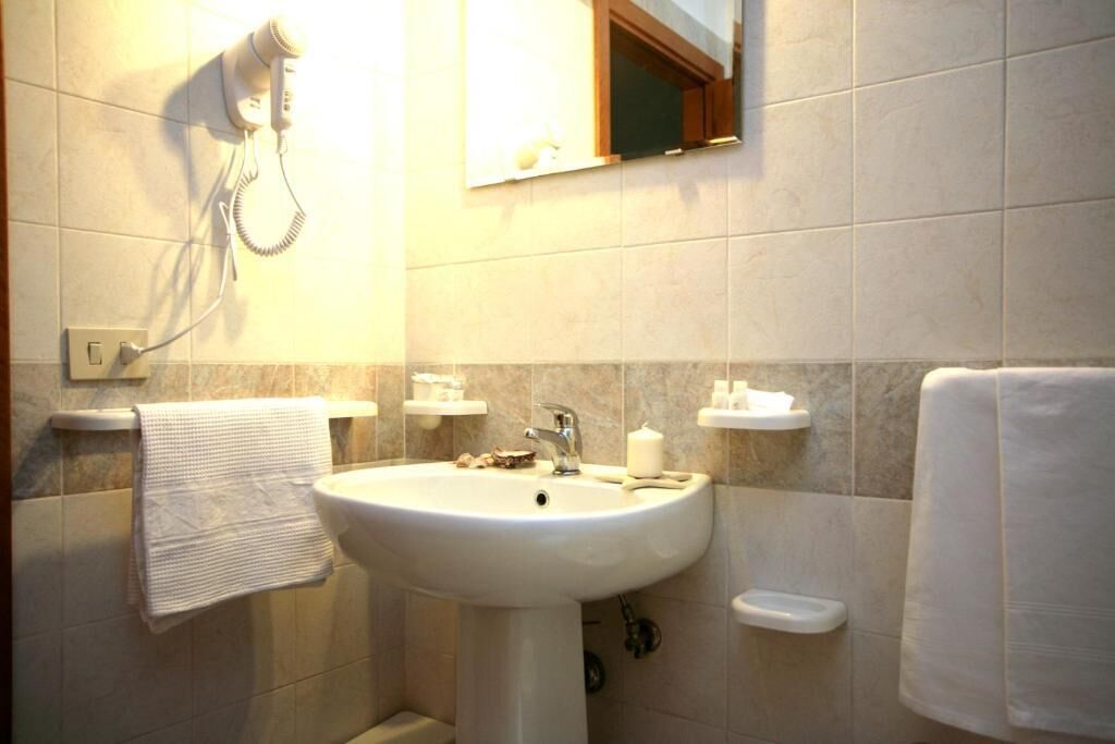 A bathroom with a white sink, a towel hanging on the wall, and a hairdryer mounted above the sink.