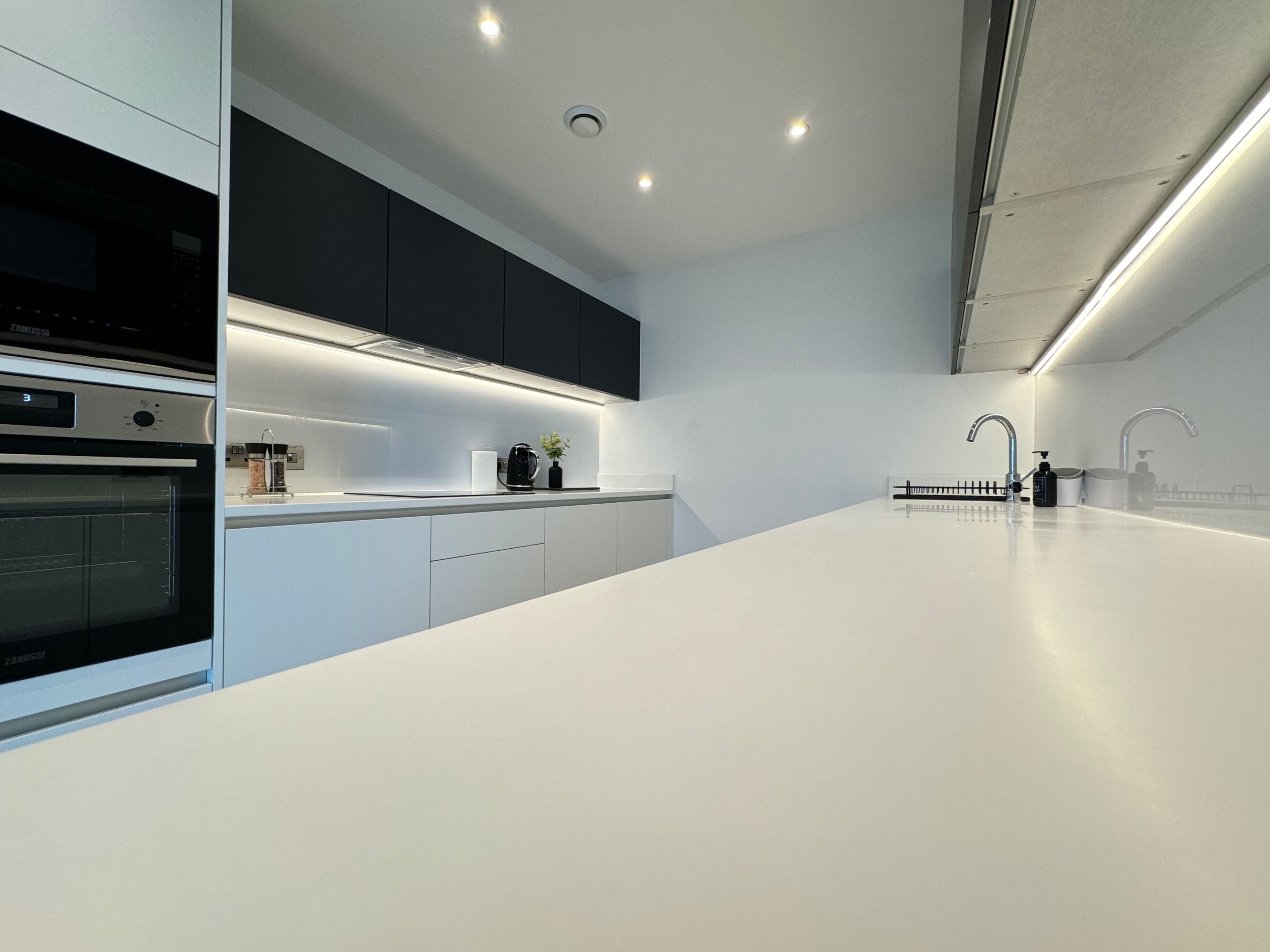 A modern kitchen with a white countertop, black cabinets, and stainless steel appliances.