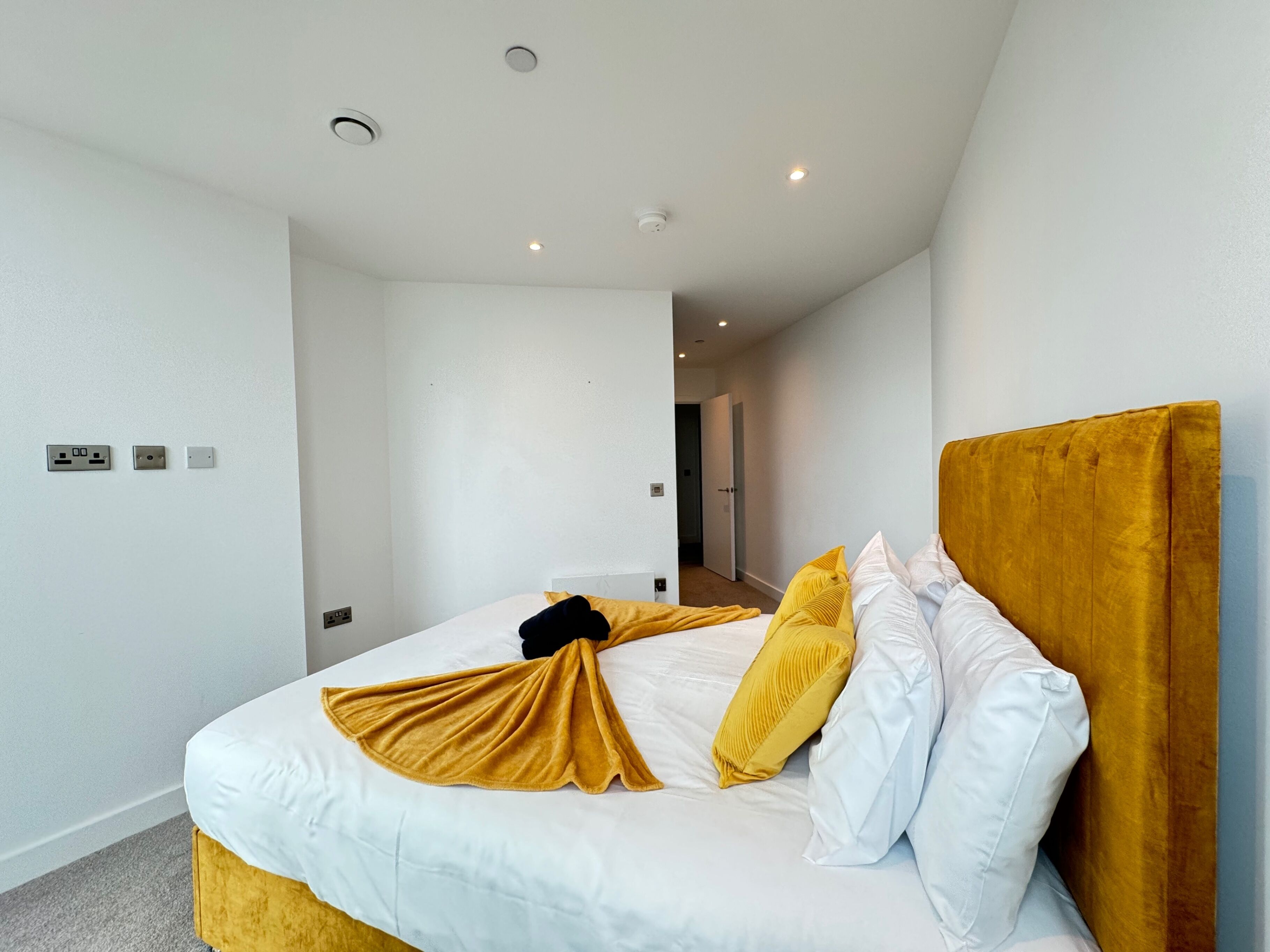 A modern hotel room with a large bed, white bedding, and a mustard-colored headboard.