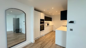 A modern kitchen with white cabinetry, a built-in oven, and a large mirror. - Manchester Oasis - Modern 3 Bedroom Apartment (Manchester)