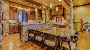 A spacious kitchen with a large island, stone walls, wooden cabinets, and hanging pendant lights. - Experience Ruidoso from the top, 360 views,private pickleball, hot tub (Ruidoso)