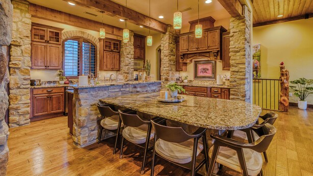 A spacious kitchen with a large island, stone walls, wooden cabinets, and hanging pendant lights. - Experience Ruidoso from the top, 360 views,private pickleball, hot tub (Ruidoso)