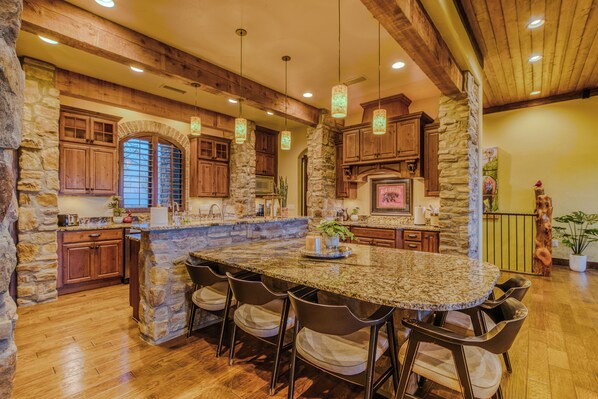 A spacious kitchen with a large island, stone walls, wooden cabinets, and hanging pendant lights. - Experience Ruidoso from the top, 360 views,private pickleball, hot tub (Ruidoso)