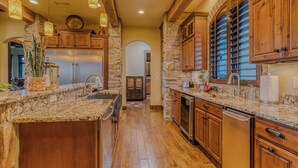 A spacious kitchen with granite countertops, wooden cabinets, and a stone accent wall. - Experience Ruidoso from the top, 360 views,private pickleball, hot tub (Ruidoso)