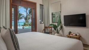 A hotel room with a large bed, a TV, a small table with a plant, and a view of the ocean through a sliding door. - The Residence: Private 3BR Beachfront Villa (Tulum)
