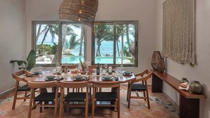A dining area with a view of the ocean, a large woven light fixture, and a textured wall hanging. - The Residence: Private 3BR Beachfront Villa (Tulum)