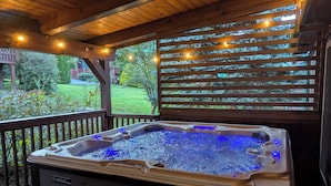 A hot tub with blue lighting, wooden deck, and a view of a garden.