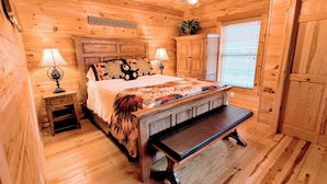 A wooden cabin bedroom with a bed, bench, ceiling fan, and a sign on the wall.
