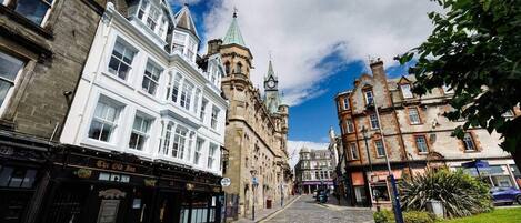 A cobblestone street lined with historic buildings, including a prominent clock tower.