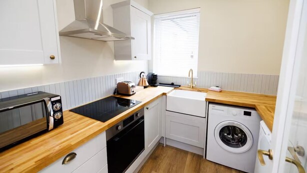 A compact kitchen with a toaster, kettle, oven, and a washing machine. - Stylish 1-bed Apartment in the Heritage Quarter (Dunfermline)