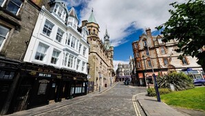 A cobblestone street lined with historic buildings, including a prominent clock tower and a pub. - Stylish 1-bed Apartment in the Heritage Quarter (Dunfermline)