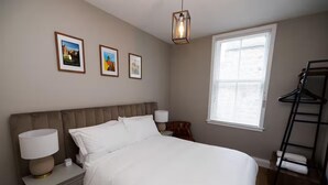 A bedroom with a bed, bedside lamps, a nightstand, a window with blinds, a hanging chair, and three framed pictures on the wall. - Stylish 1-bed Apartment in the Heritage Quarter (Dunfermline)