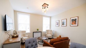 A living room with a sofa, armchairs, a coffee table, and a TV mounted on the wall. - Stylish 1-bed Apartment in the Heritage Quarter (Dunfermline)