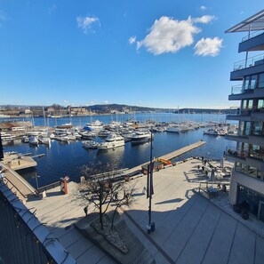 A marina with multiple boats docked, a clear sky, and a view of a distant cityscape.