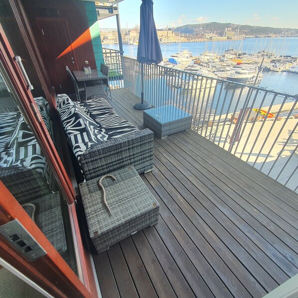A balcony with wicker furniture, a view of a marina with boats, and a distant cityscape.