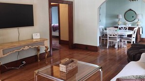 Ein Wohnzimmer mit Fernseher, einem Holz-Konsolentisch, einem Glastisch und einem Essbereich mit weißen Stühlen und einem Tisch.