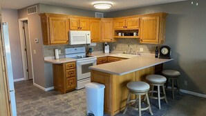 A kitchen with wooden cabinets, a white stove, a microwave, a sink, and a large island with stools. - Spacious 2-bedroom condo with AC, WiFi in beautiful Osage Beach (Osage Beach)