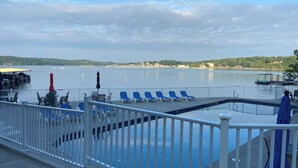 A deck with blue lounge chairs and a pool, overlooking a calm lake with boats and a distant shoreline. - Spacious 2-bedroom condo with AC, WiFi in beautiful Osage Beach (Osage Beach)