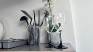Een tafel met twee glazen wijn, een metalen houder met bestek, en een witte orchidee.
