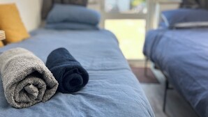 Een hotelkamer met twee bedden, elk met een blauwe spreidek en kussens. Er liggen handdoeken op de bedden, en vanuit de kamer is uitzicht door een raam.