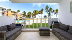 Ein Balkon mit Korbmöbeln, Blick auf einen Pool und Palmen.