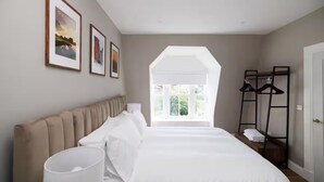 A bedroom with a large bed, a window, a coat rack, and framed pictures on the wall. - Cosy Apartment in the Heritage Quarter - Sleeps 2 (Dunfermline)