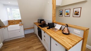 A compact kitchen with wooden countertops, a coffee machine, and a kettle. There are three framed pictures on the wall. - Cosy Apartment in the Heritage Quarter - Sleeps 2 (Dunfermline)