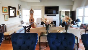 Un salon comprenant un canapé, des fauteuils, une table à manger, une horloge, un téléviseur et des œuvres d’art accrochées aux murs.