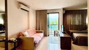 A modern hotel room with a sofa, a small table, a TV, and a view of the outdoors. - Loft with pool - Near Riocentro and Barra (Rio de Janeiro)