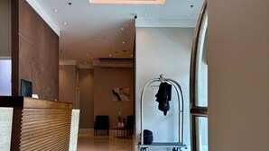 A modern hotel lobby with a reception desk, a seating area, and a luggage cart. - Loft with pool - Near Riocentro and Barra (Rio de Janeiro)