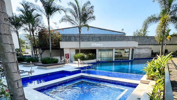 A swimming pool area with a modern building in the background, surrounded by palm trees and plants. - Loft with pool - Near Riocentro and Barra (Rio de Janeiro)