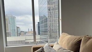 A bedroom with a large window, a bed with multiple pillows, and a view of city buildings. - Downtown Suite - Stunning View Right in the centre of Edmonton (Edmonton)