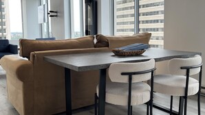 A modern living room with a sofa, a dining table, and chairs. There are large windows providing a view of the city. - Downtown Suite - Stunning View Right in the centre of Edmonton (Edmonton)