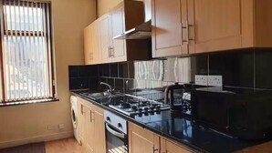 A modern kitchen with wooden cabinets, a black countertop, and a window with blinds. - Bradford 2-bedroom Home - Sleeps 4 - Free Parking (Bradford)