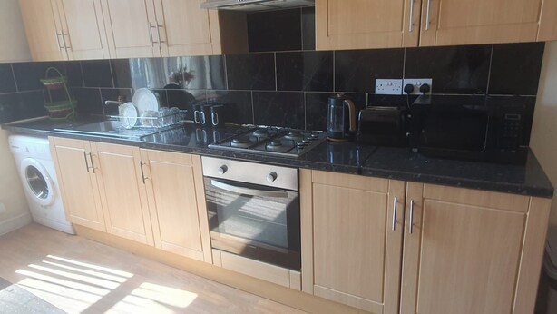 A kitchen with wooden cabinets, a stainless steel range hood, a built-in oven, and a washing machine. - Bradford 2-bedroom Home - Sleeps 4 - Free Parking (Bradford)